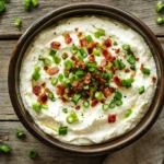 Bowl of bacon scallion cream cheese on a rustic wood board with a spoon