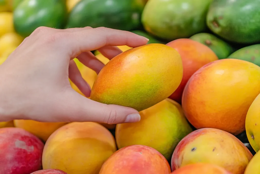 A hand selecting ripe mangoes at a grocery store